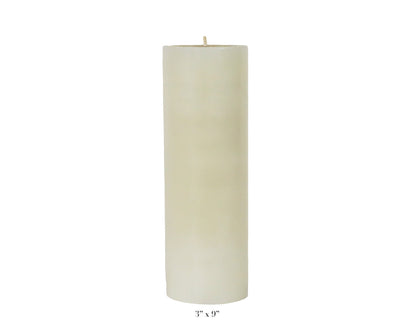 A Perin Mowen Solid Pillar Candle Collection piece—a tall white beeswax candle (3" diameter, 9" height)—is shown against a plain white background, showcasing the warm glow of natural candlelight.