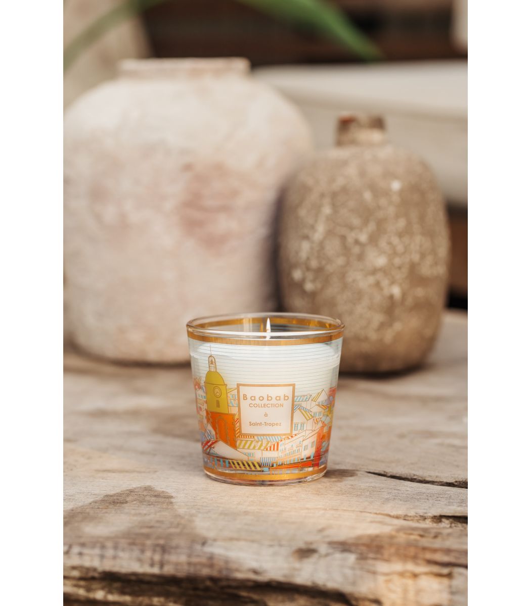 A Baobab Collection Saint Tropez candle by Baobab in a glass holder with orange accents infuses the air with a summery scent, while two textured vases in the background enhance the decor.