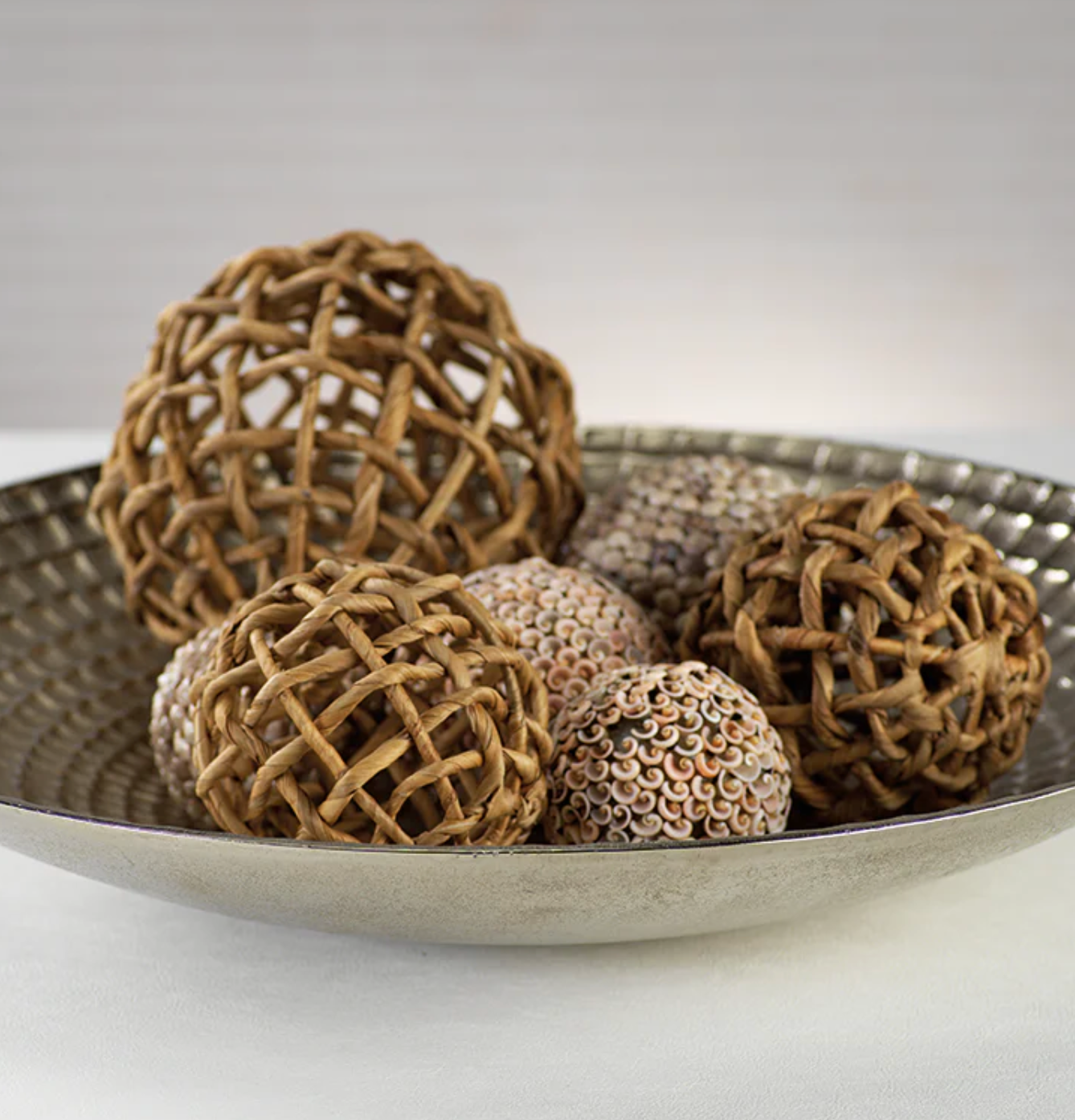 The Zodax Water Hyacinth Twisted Fill Ball Collection features decorative spheres in a silver bowl, perfect for adding natural woven style to your home or garden décor.