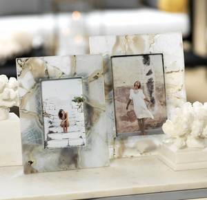 Two Zodax Preto Agate Frames display outdoor photos of women on a marble surface, surrounded by white coral decor, highlighting the unique beauty of these decorative photo frames.