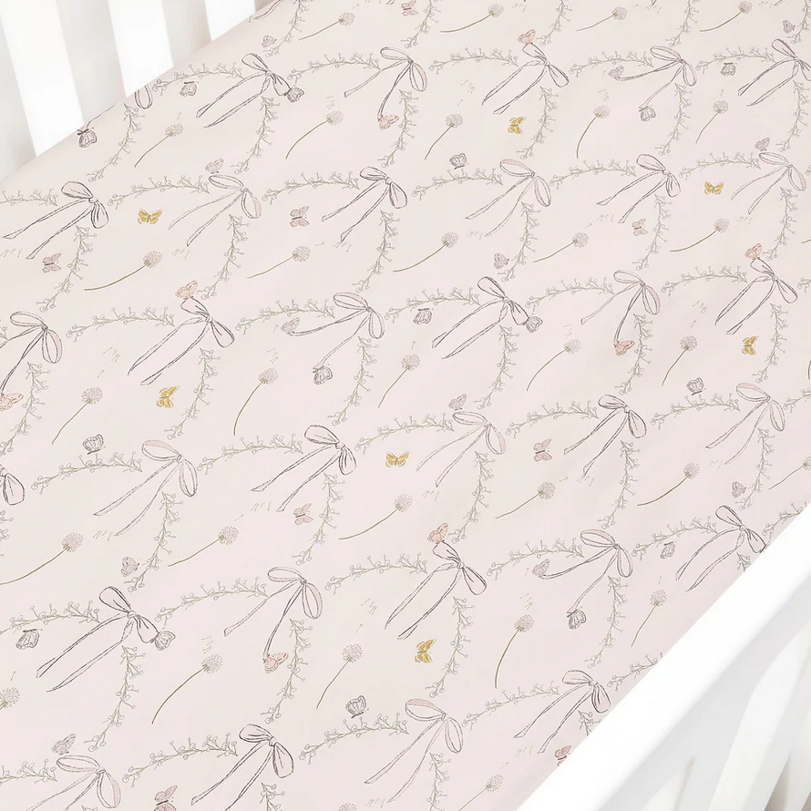 The Gooselings Bows & Butterfly Kisses Bedding Collection fitted crib sheet showcases a light pink background adorned with a charming repeat of bows, garlands, butterflies, and delicate flowers in soft pastel hues. Made from pure materials and OEKO-TEX certified for your peace of mind, this sheet offers a gentle and breathable surface to ensure your little one sleeps comfortably.