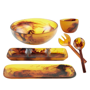 The Tortoise Resin Serveware Collection by Nashi Home features amber and brown marbled serving pieces—large bowl, small bowl, divided tray, platter, and salad utensils—that are stylish, shatter resistant, and perfect for daily use.