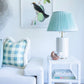 A living room featuring the Herend Reserve Collection Nautilus, Multicolor, adds artistic flair with its hand-painted designs showcased alongside a light blue sofa, plaid cushion, side table, blue lamp, books, and bird artwork.
