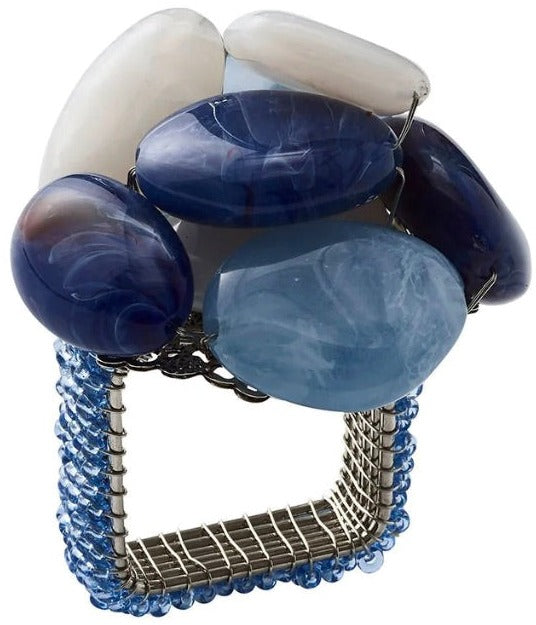 The Kim Seybert Sea Stone Napkin Ring features a square metal design with blue beads and large blue and white polished beach stones for a chic, coastal look.