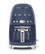 A blue Smeg Drip Filter Coffee Machine Collection with a glass carafe, digital display, reusable filter, and silver accents sits against a white background. It includes a keep-warm function for convenience.