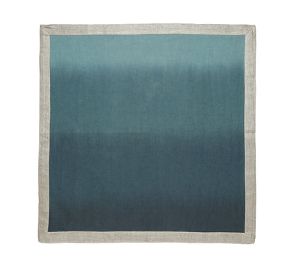 The Kim Seybert Dip Dye Napkin Set features rectangular napkins with a beige border and a blue ombre center, hand-dipped to fade from light blue at the top to dark blue at the bottom.