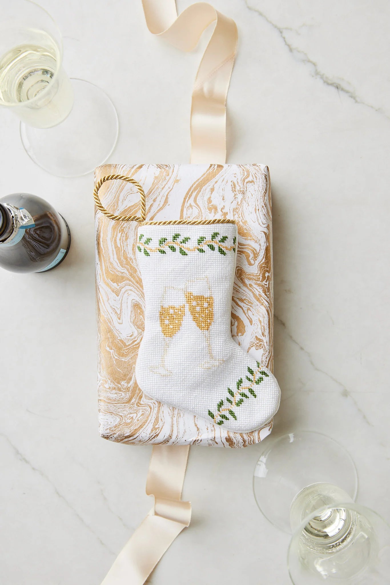 Gift-ready in a white and gold marbled box, the Bauble Stockings Champagne Toast Needle Point Stocking features hand-stitched champagne glasses—an embroidered keepsake ornament perfect for festive celebrations.