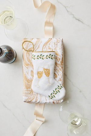 Gift-ready in a white and gold marbled box, the Bauble Stockings Champagne Toast Needle Point Stocking features hand-stitched champagne glasses—an embroidered keepsake ornament perfect for festive celebrations.
