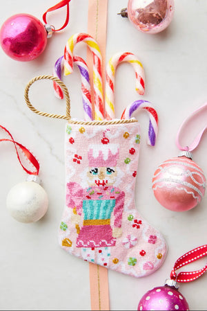 The Sugary Sweet Pink Nutcracker Needle Point Stocking by Bauble Stockings features striped candy canes and pink, white, and red ornaments—perfect festive holiday decor for a white surface.