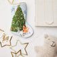 The Woodland Creatures Needle Point Stocking by Bauble Stockings, paired with gold star ornaments, a plush bear, a pearl necklace, and a closed book, creates a charming and festive holiday display on any white surface.