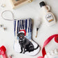 The Woodland Frolic Needle Point Stocking by Bauble Stockings features a hand-stitched black dog in a Santa hat surrounded by festive ribbons, a bottle, small bells, and decorative accents on a white background.