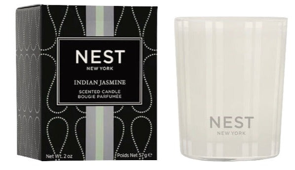 A Nest Indian Jasmine Votive Candle next to its packaging, featuring a clear glass holder and a black box with decorative patterns.