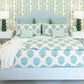A Lee Industries Flair King Bed with a light blue upholstered frame, dressed in a white duvet and shams featuring Solstice Beach fabric, centered between two nightstands with green lamps.