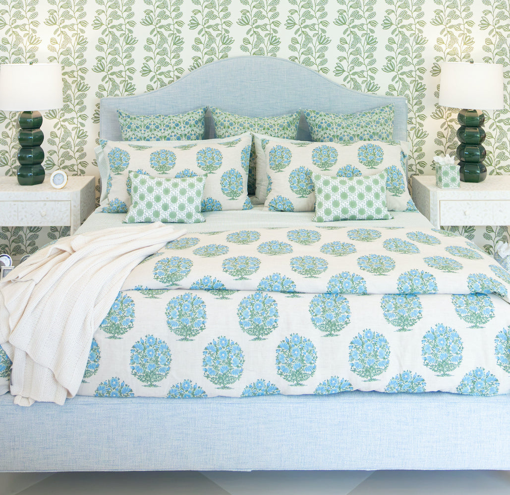 A Lee Industries Flair King Bed with a light blue upholstered frame, dressed in a white duvet and shams featuring Solstice Beach fabric, centered between two nightstands with green lamps.