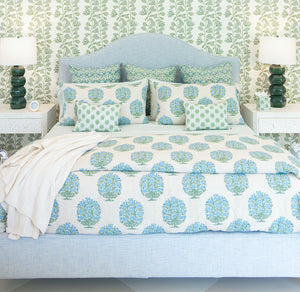 A Lee Industries Flair King Bed with a light blue upholstered frame, dressed in a white duvet and shams featuring Solstice Beach fabric, centered between two nightstands with green lamps.