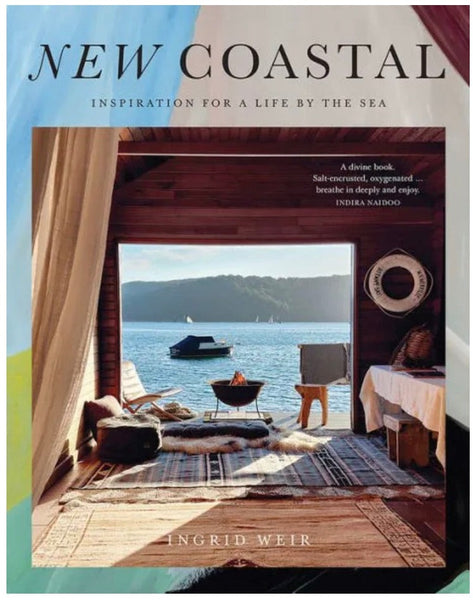 Cover of the book "New Coastal: Inspiration for a Life by the Sea" by Ingrid Weir, featuring an open wooden interior leading to a view of the sea with boats. The cover blurb describes this exploration of coastal living as a divine and inspiring read. Chronicle Books.