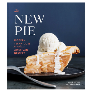 A slice of apple pie topped with melting vanilla ice cream rests on a black plate on the cover of The New Pie, a cookbook from Penguin Random House that highlights inventive pie recipes and creative baking techniques.