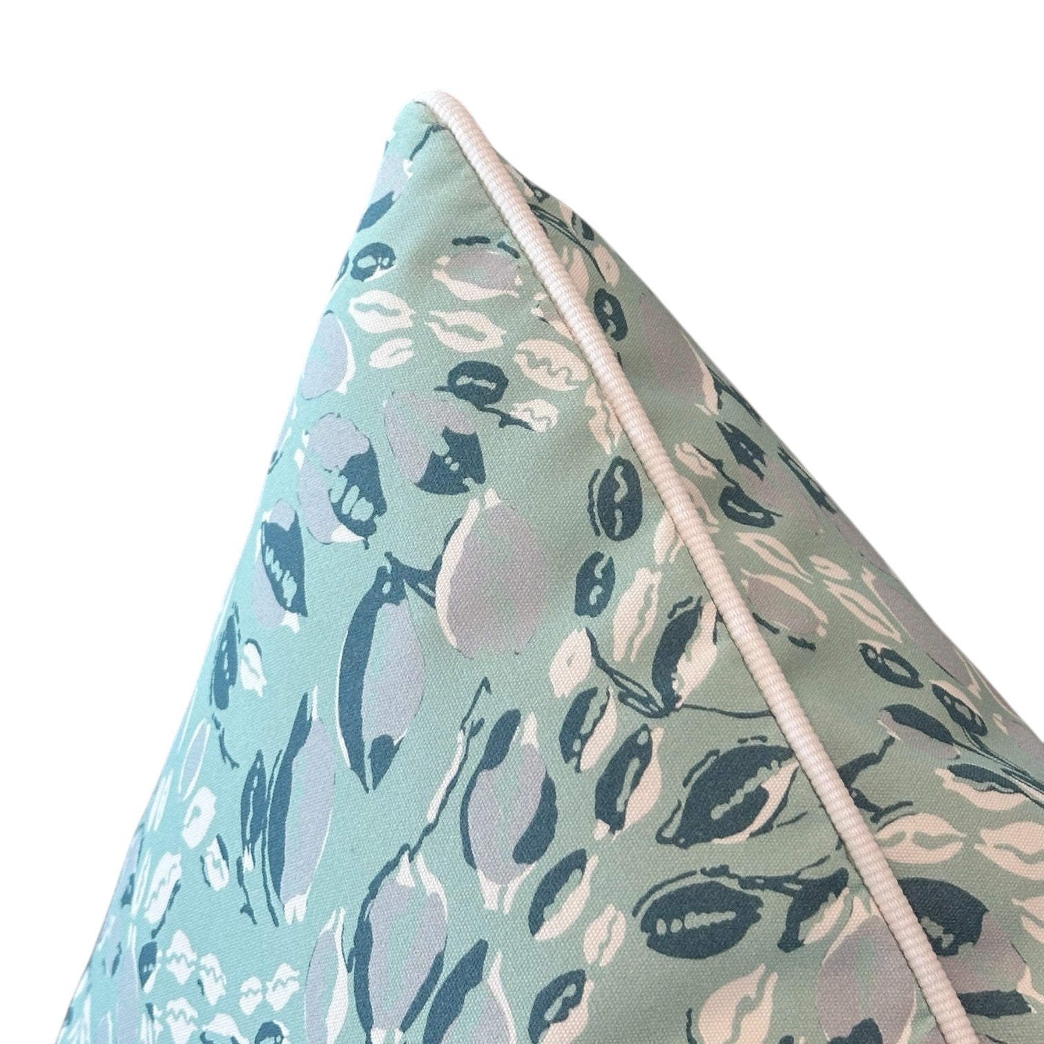 Close-up of the Cowrie Shell Aqua Outdoor Pillow by Associated Design, featuring a white piped edge and abstract leaf shapes in white, blue, and gray on light blue-green, crafted from premium materials.