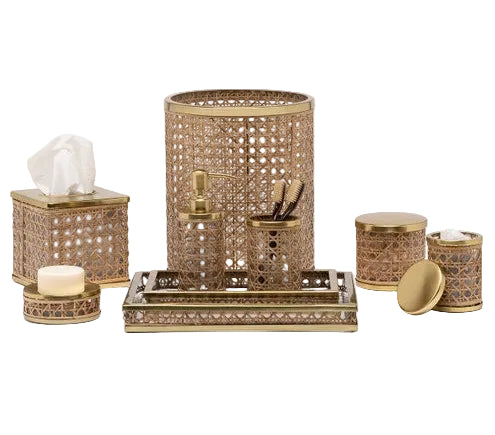 The Norwell Bath Collection by Pigeon & Poodle displays gold and brown woven rattan accessories—tissue box, waste bin, soap dish, tray, and jars—elegantly arranged on a white background.