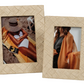 Two woven raffia frames from the Zodax La Bocca Frame Collection add natural chic charm—one displays a sunbathing woman on the beach, the other features a woman indoors with an orange shawl.