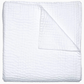 A neatly folded white chambray quilt from the Vivada Bedding Collection by John Robshaw features a textured, grid-like pattern; one corner is turned over to showcase its reversible design and the fine hand-stitched detailing on the underside.