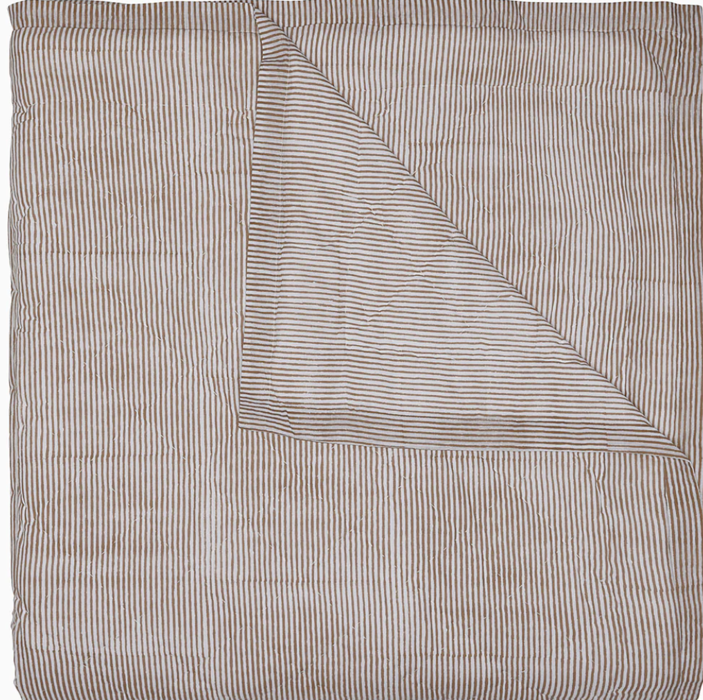From the John Robshaw Nandi Bedding Collection, a striped cotton quilt is folded at one corner to reveal the reverse, with both sides displaying narrow horizontal and vertical stripes in neutral tones and beautifully hand-quilted for added texture.