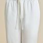 Close-up of a person's lower torso wearing loose-fitting white Fifi Silk Pajama pants by Olivia von Halle, featuring an elastic waistband and tied drawstring.