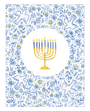 The Menorah and Doves Boxed Card Set by Caspari features a golden menorah with eight blue candles and one yellow candle, centered in a floral and dove-patterned blue and white border—making it an ideal choice for greeting cards crafted on FSC-certified cardstock.