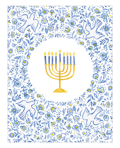 The Menorah and Doves Boxed Card Set by Caspari features a golden menorah with eight blue candles and one yellow candle, centered in a floral and dove-patterned blue and white border—making it an ideal choice for greeting cards crafted on FSC-certified cardstock.