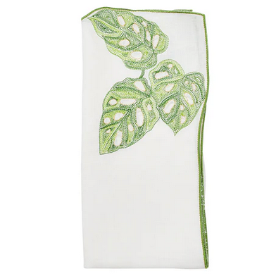 The Kim Seybert Calypso Napkin Set includes 4 white linen napkins, each embroidered with green monstera leaves and finished with a matching green border along one edge.