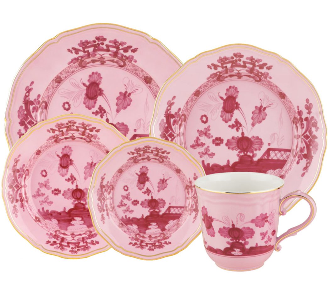 The Oriente Italiano Porpora Dinnerware Collection by Ginori 1735 features pink and white porcelain with floral and lattice motifs, including assorted plates and a gold-trimmed teacup, inspired by Italian elegance.