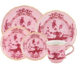 The Oriente Italiano Porpora Dinnerware Collection by Ginori 1735 features pink and white porcelain with floral and lattice motifs, including assorted plates and a gold-trimmed teacup, inspired by Italian elegance.