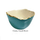 A small bowl from Beatriz Ball's Encanto Turquoise Serveware Collection features a glossy teal enameled aluminum exterior, cream interior, and gold-rimmed edge. Text below reads "Osaka Small Bowl.