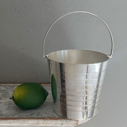 A Hôtel Silver Vintage Ice Pail with a hinged handle sits on a wooden surface beside a whole lime.