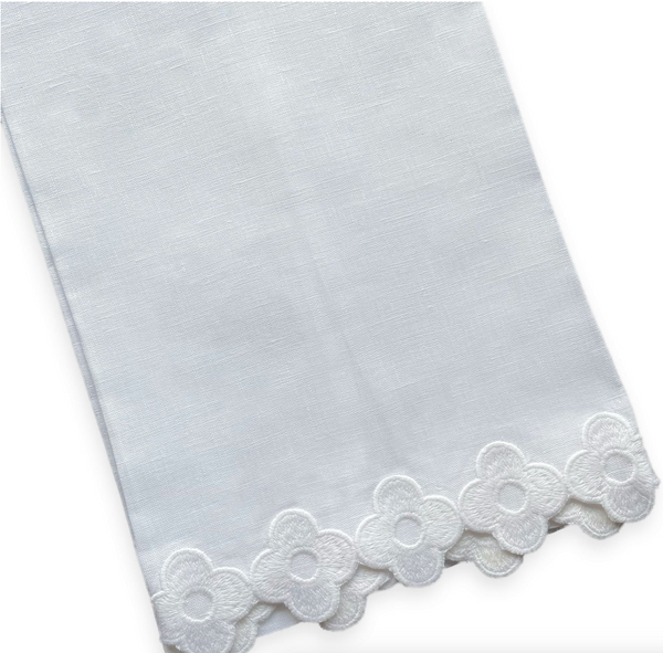 The "Dolly Tip Towel" by Haute Home is a 14" x 20" linen piece in white fabric with a floral lace edge, showcasing hand-embroidered flower patterns along one side.