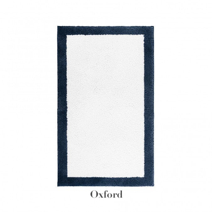 Rectangular white Egoist Border Bath Rug by Graccioza, featuring a thick dark border and subtle brand label. Made from Egyptian cotton with a non-slip silicone coating for enhanced safety.