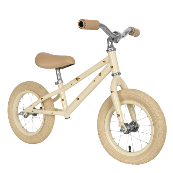 The Konges Slojd Balance Bike by Konges Slojd is a beige children's balance bicycle with a sturdy steel frame, brown handlebar grips, and seat. This lightweight design has no pedals and features small bee decorations on the frame and tires.