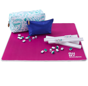 The Oh My Mahjong Palm Beach Mahjong Travel Set features a magenta case, white rack, tiles, dice, and two zippered pouches—one white with a blue pattern and one solid blue—arranged on a white background for travel play.