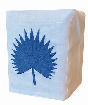 Haute Home’s Palm Leaf Bath Collection features a white Italian linen tissue box cover adorned with a blue embroidered palm leaf on the front.