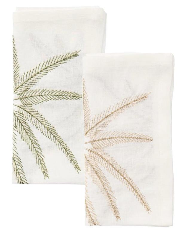 The Kim Seybert Palm Coast Napkin Set includes two folded white linen napkins, each adorned with a green and tan embroidered palm frond—an elegant touch for your coastal dining table.