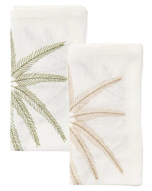 The Kim Seybert Palm Coast Napkin Set includes two folded white linen napkins, each adorned with a green and tan embroidered palm frond—an elegant touch for your coastal dining table.