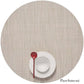 A white plate and bowl with a red spoon sit on a round Chilewich placemat in Parchment, featuring a Mini Basketweave design made from Terrastrand yarns. This phthalate-free placemat ensures safe, stylish dining.