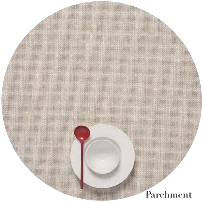 A white plate and bowl with a red spoon sit on a round Chilewich placemat in Parchment, featuring a Mini Basketweave design made from Terrastrand yarns. This phthalate-free placemat ensures safe, stylish dining.