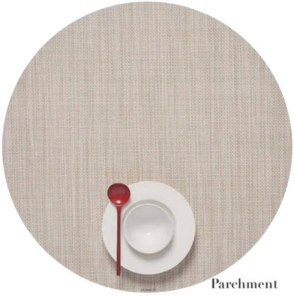 A white plate and bowl with a red spoon sit on a round Chilewich placemat in Parchment, featuring a Mini Basketweave design made from Terrastrand yarns. This phthalate-free placemat ensures safe, stylish dining.