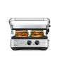 The Breville Sear & Press Grill is grilling two sandwiches; visible control knobs and indicator lights are on the front panel of this stainless steel panini press.