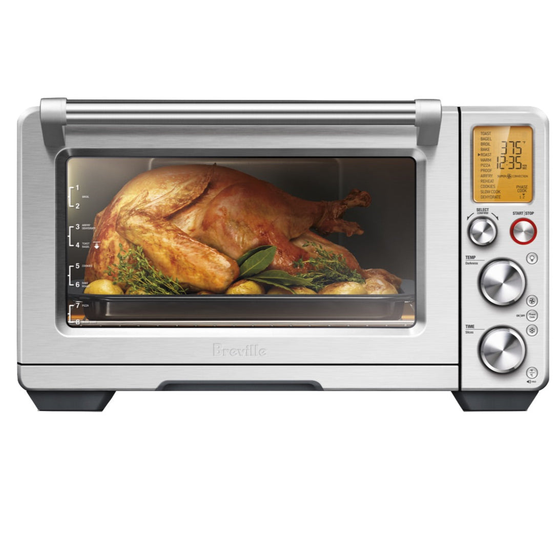 A whole roasted chicken with vegetables is inside the Breville Smart Oven Air Fryer Pro, visible through the glass door with the controls and temperature display on the right.