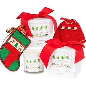 The Perfectly Palm Beach Holiday Candle set features two boxed candles with red ribbons, a festive green and red ornament stocking, and a sheep-adorned red pouch—perfect for adding an evergreen touch to the holiday season.