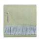 A folded light green Classic Herringbone Throw by Alicia Adams Alpaca, featuring light blue fringes and a fabric label on one side, ethically made in Peru.
