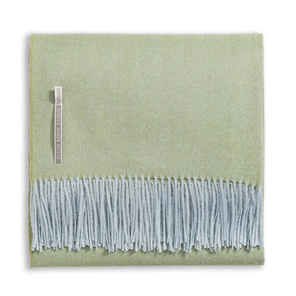 A folded light green Classic Herringbone Throw by Alicia Adams Alpaca, featuring light blue fringes and a fabric label on one side, ethically made in Peru.
