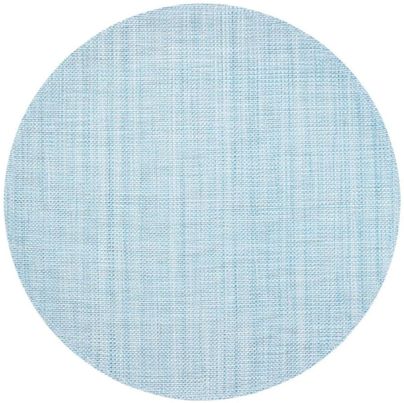 The Kim Seybert Portofino Placemat features a round, light blue design with a subtle woven vinyl texture and faint intersecting lines, and is easy to clean.
